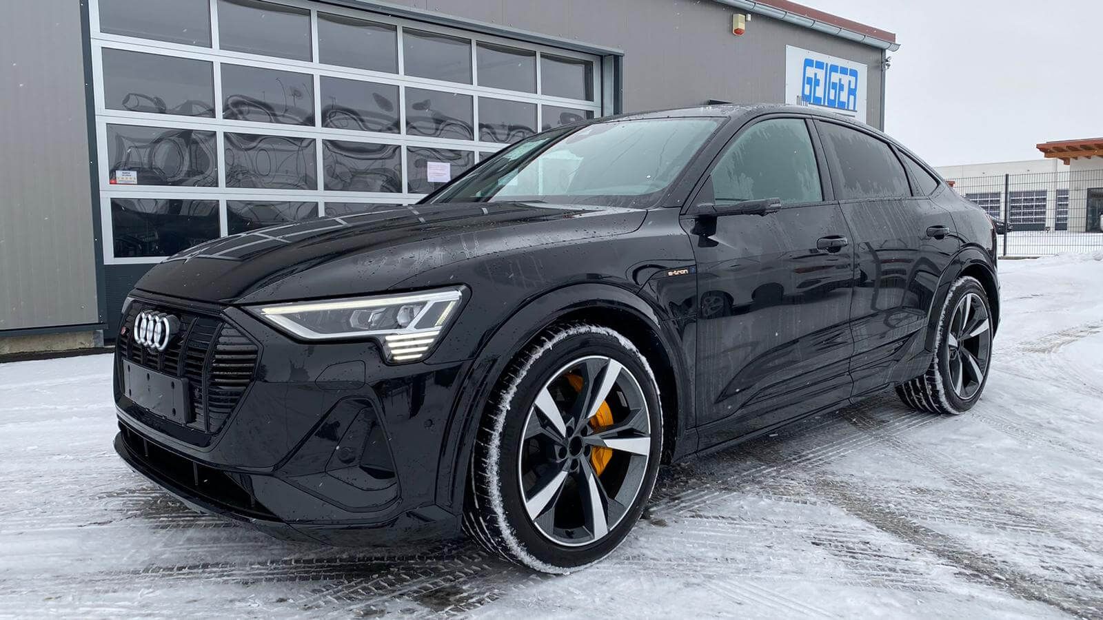Svart Audi e-tron Sportback på snødekt plass foran et forhandlerbygg